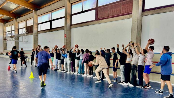 Grupo de jóvenes practicando baloncesto en un gimnasio bajo la supervisión de entrenadores.