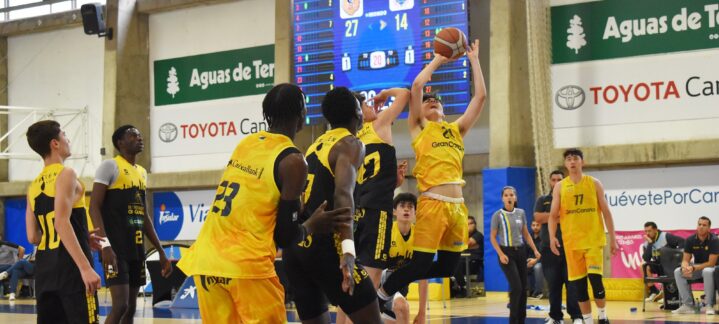Jugadores compiten en un partido de baloncesto, uno lanza a canasta en el local.