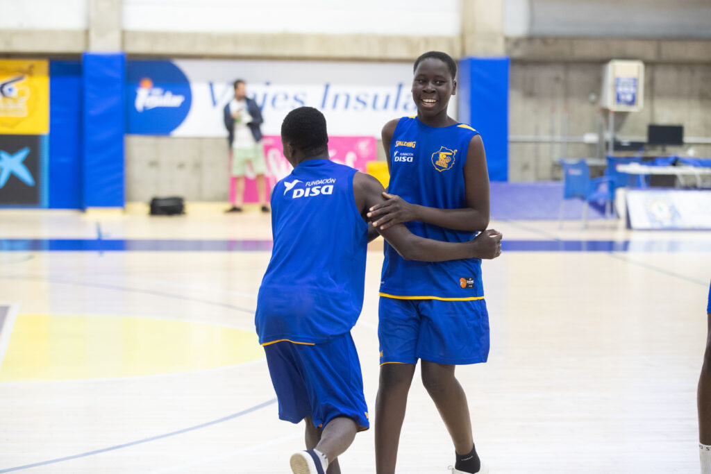 Dos jóvenes jugadores de baloncesto sonríen y se abrazan en la cancha.