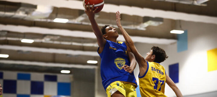 Jugadores en un entrenamiento de baloncesto, uno realizando un tiro y otro defendiendo.