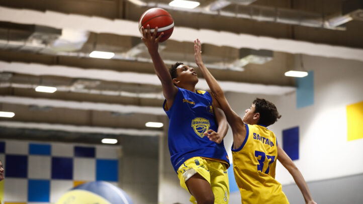 Jugadores en un entrenamiento de baloncesto, uno realizando un tiro y otro defendiendo.