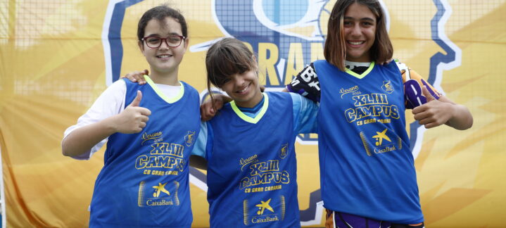 Tres niños sonrientes muestran pulgares hacia arriba, luciendo camisetas del Campus de Verano.