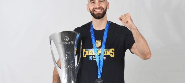 Jugador sonriente sosteniendo un trofeo y medalla, celebrando un logro deportivo.