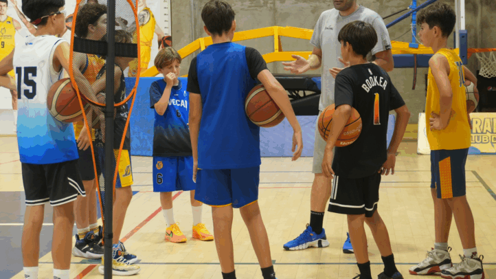 Grupo de jóvenes escuchando a un entrenador durante un evento de formación de baloncesto.