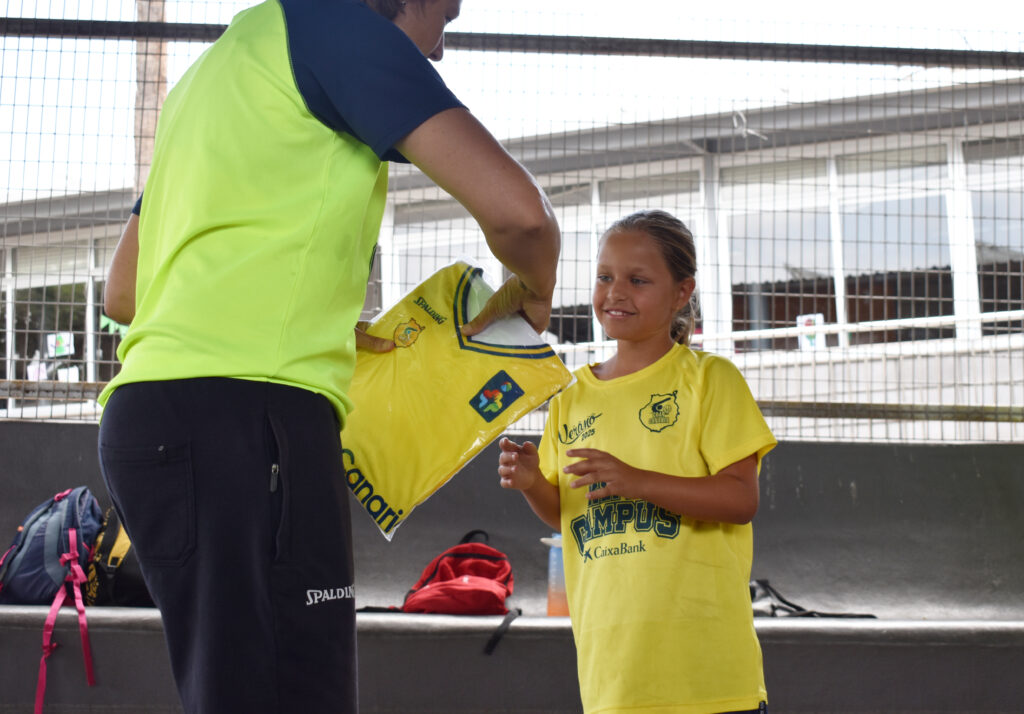 Niña sonriente recibe una camiseta del Club Baloncesto Gran Canaria durante el campus.