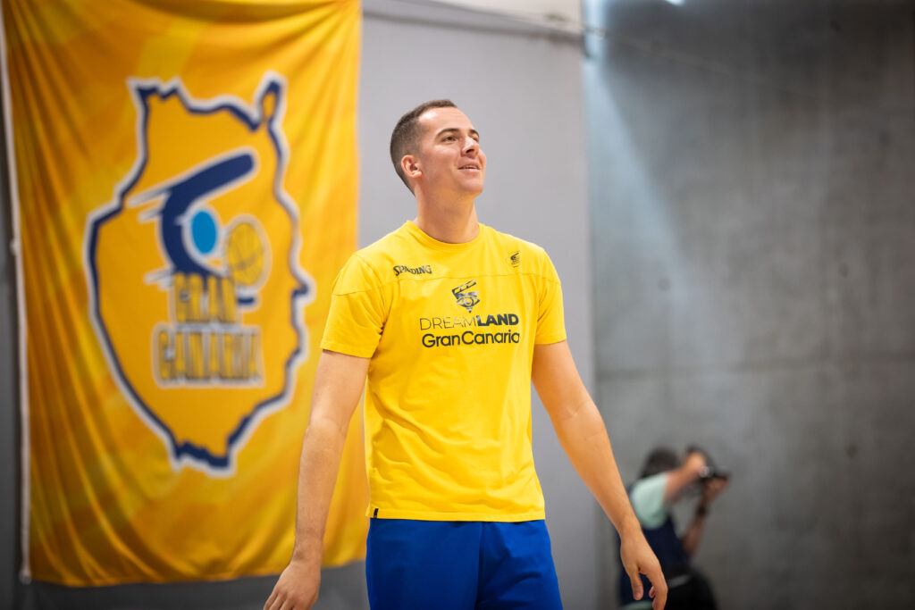 Jugador del Dreamland Gran Canaria sonríe durante un entrenamiento, con fondo amarillo.