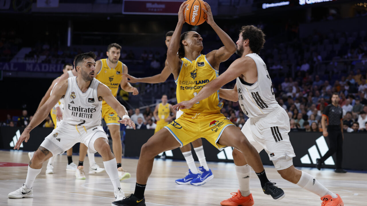 Jugadores de baloncesto en acción, con uno intentando encestar bajo la defensa rival.