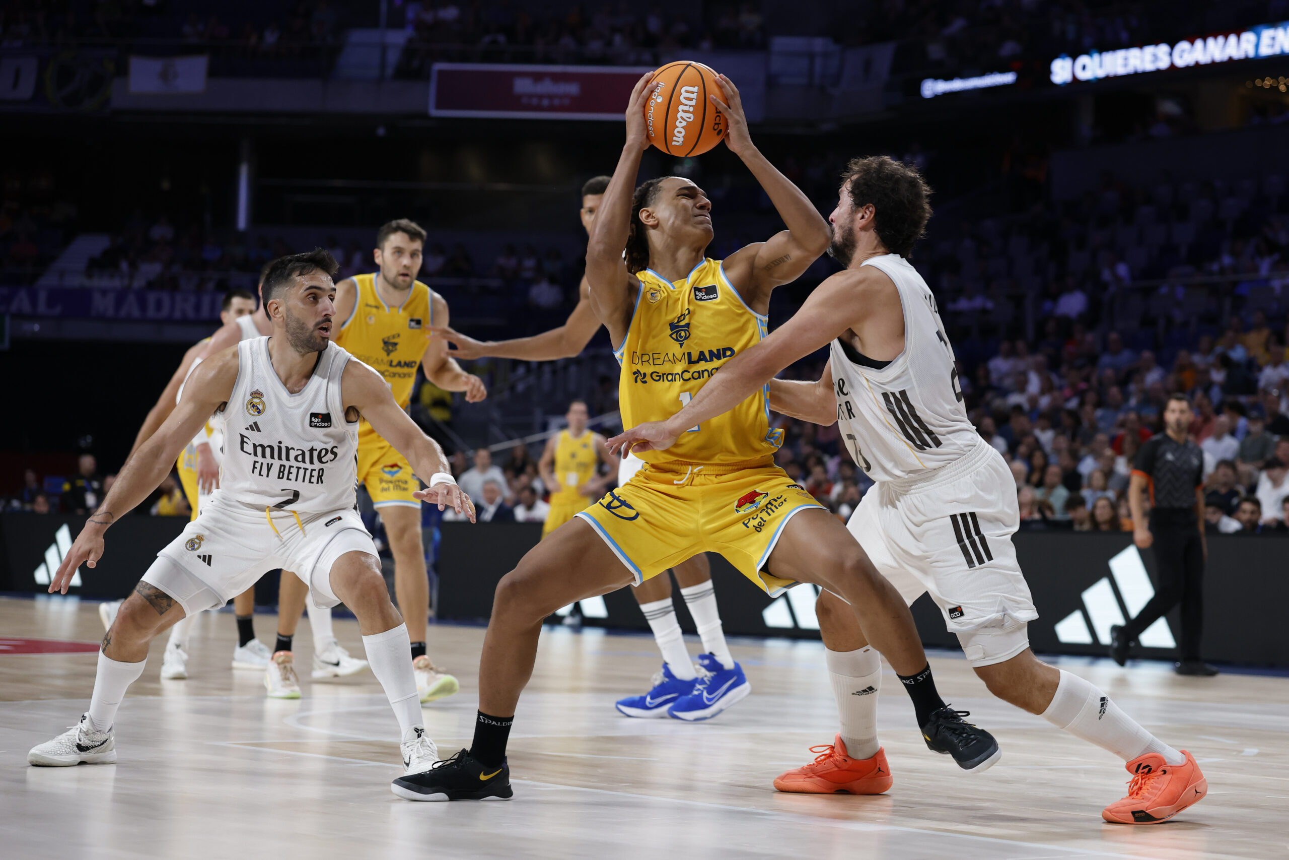 Jugadores de baloncesto en acción, con uno intentando encestar bajo la defensa rival.