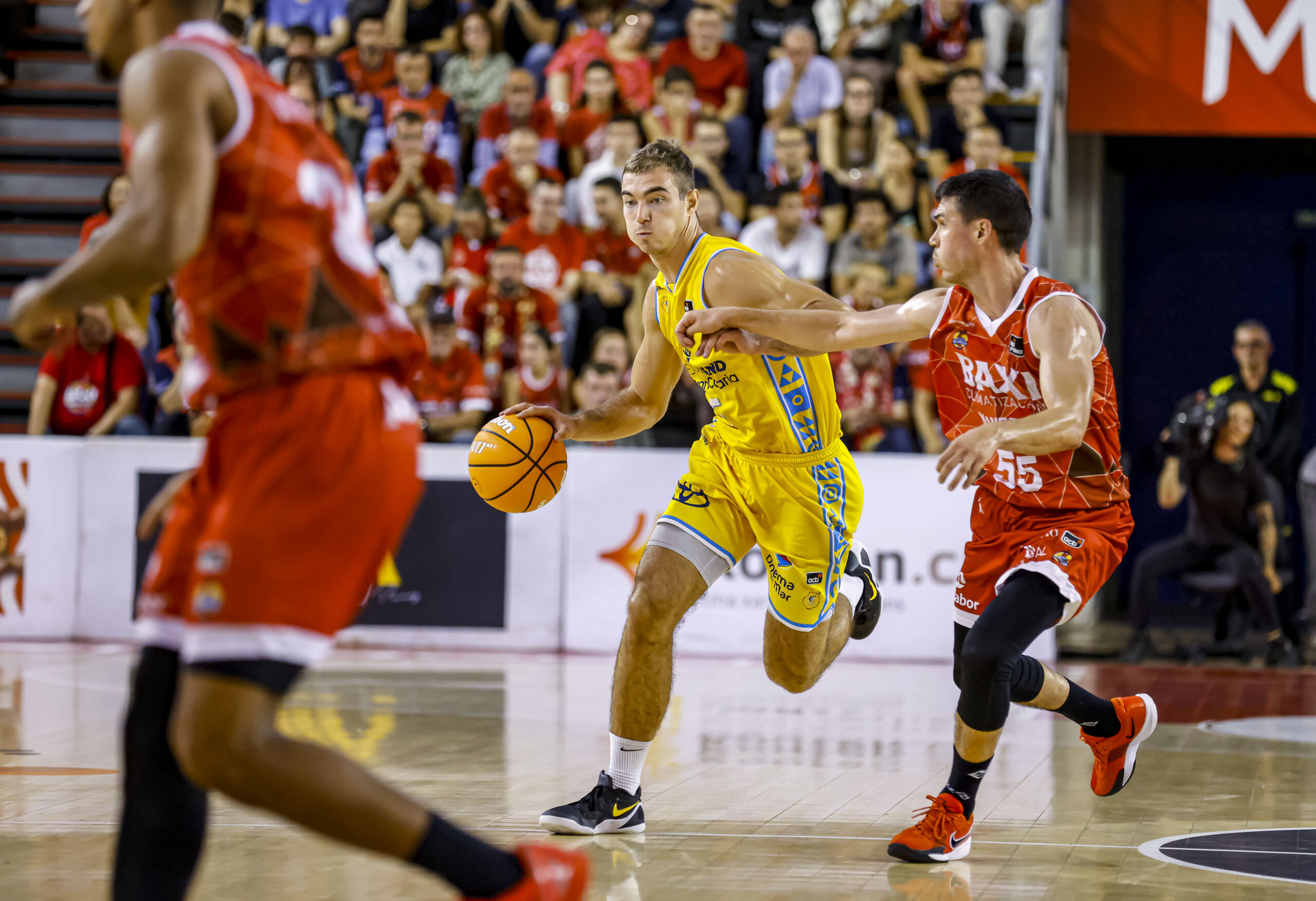Jugadores de baloncesto compiten, uno driblando y el otro en defensa durante un partido.