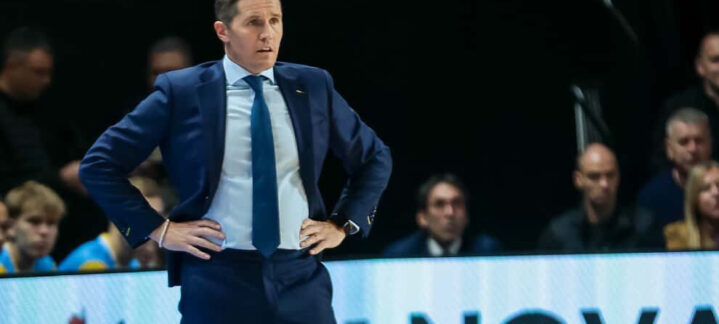 Entrenador de baloncesto observando el juego en un partido, con una actitud concentrada.