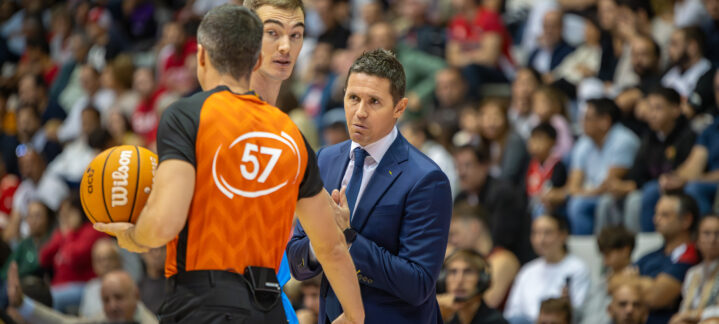 Jaka Lakovic conversa con un árbitro y un jugador durante un partido de baloncesto.